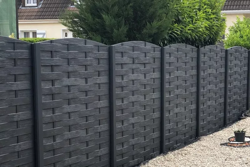clôture en béton imitation bois tressé avec arrondie de couleur anthracite le long d'une allée gravillonnée